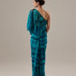 Woman wearing a teal tie-dye one-shoulder dress against a beige background