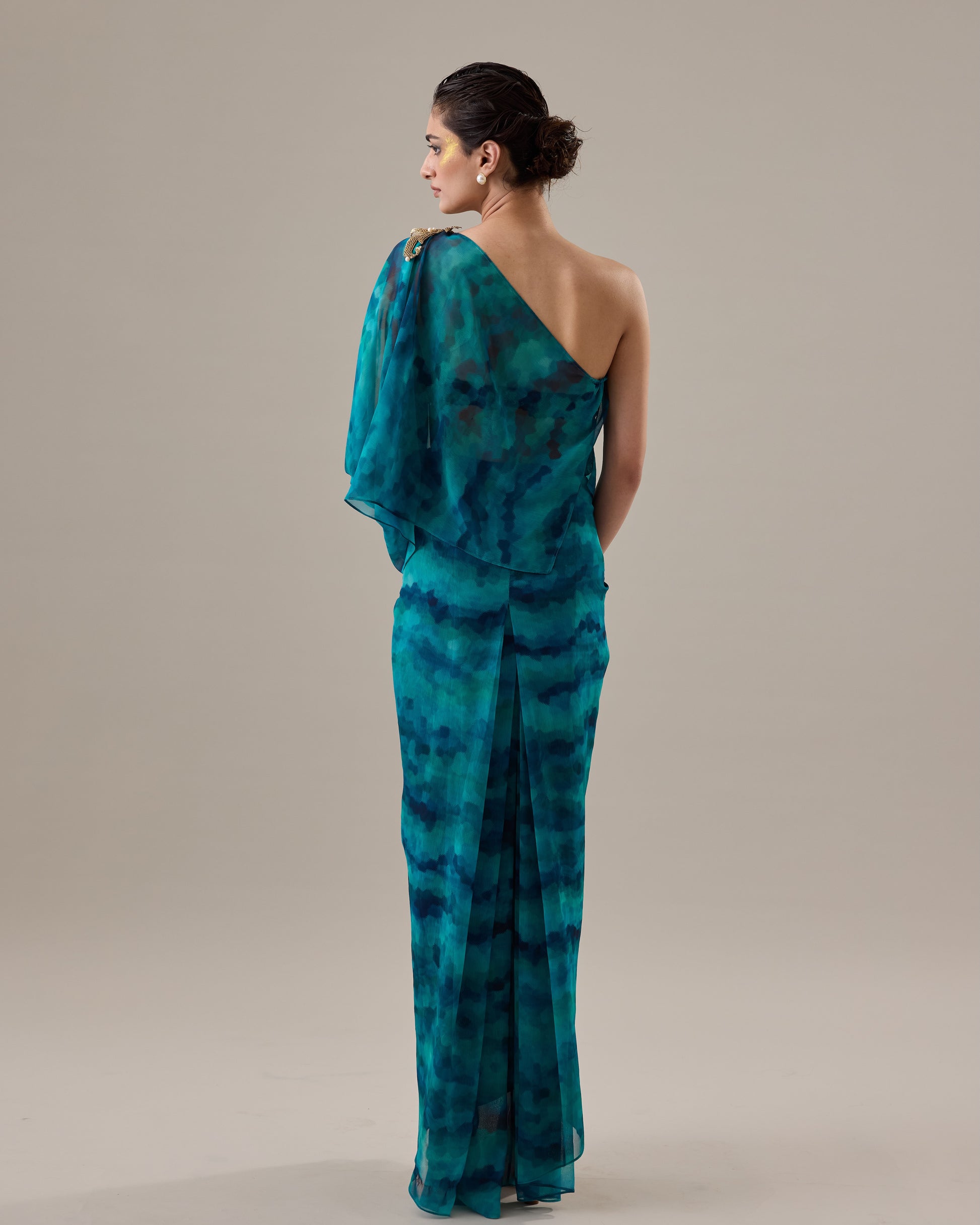 Woman wearing a teal tie-dye one-shoulder dress against a beige background
