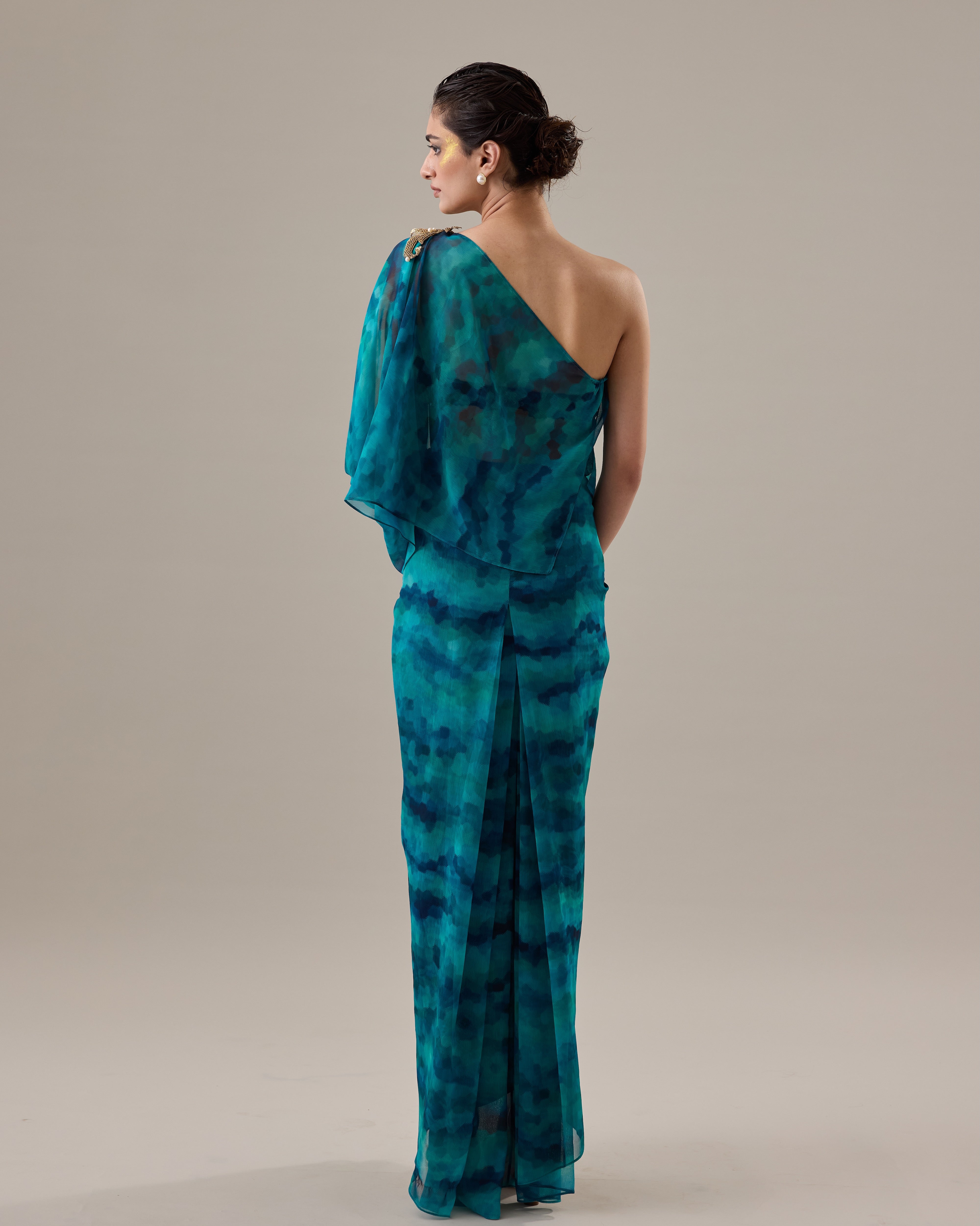 Woman wearing a teal tie-dye one-shoulder dress against a beige background