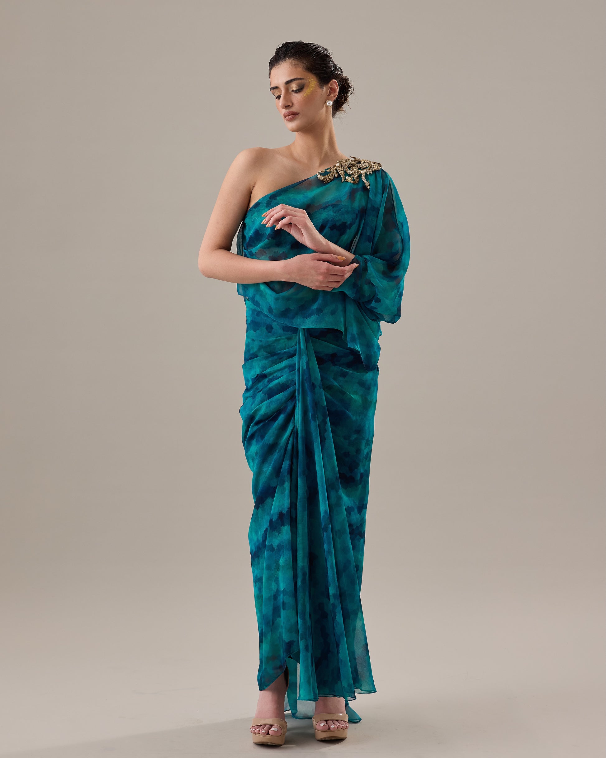Woman wearing a teal one-shoulder dress against a plain background